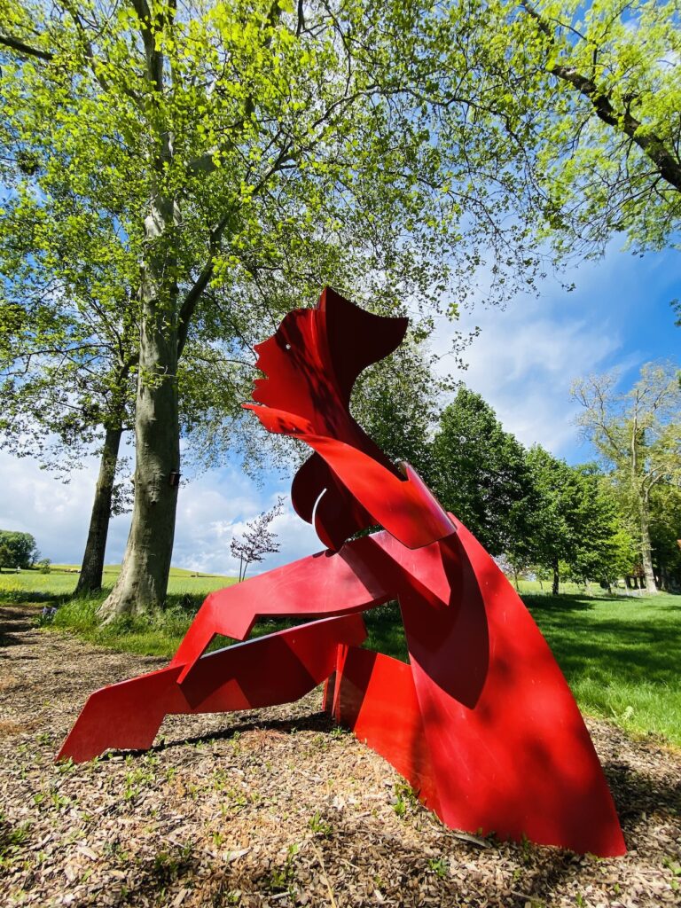 Sculpture d'un rouge vif, de l'artiste Allen Jones, exposée sous des arbres, au domaine du Château de Vullierens.