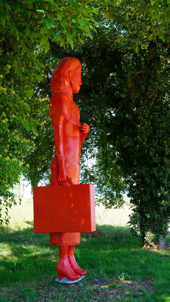 Oeuvre géante "la gardienne du Temps" de Catherine Gfeller représentant une femme asiatique, de couleur rouge vif, debout en train de porter une valise.