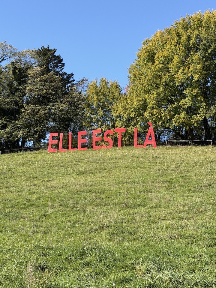 "Elle est là" écrit en rouge sur des lettres géantes, à côté de la sculpture de Catherine Gfeller.