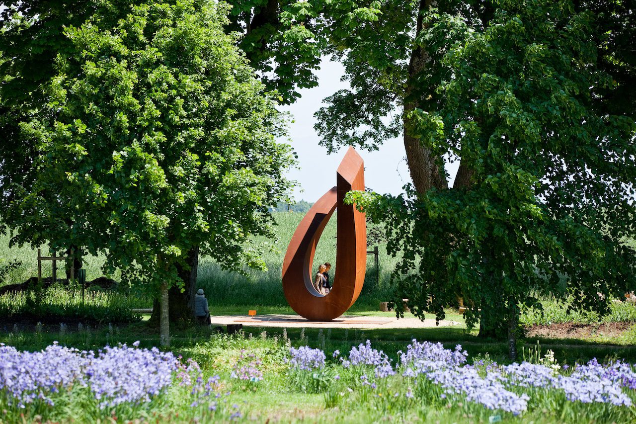 Plan large du jardin de Muni du Château de Vullierens en avril, il y a des visiteurs qui marchent à côté des sculptures monumentales de ce jardin.