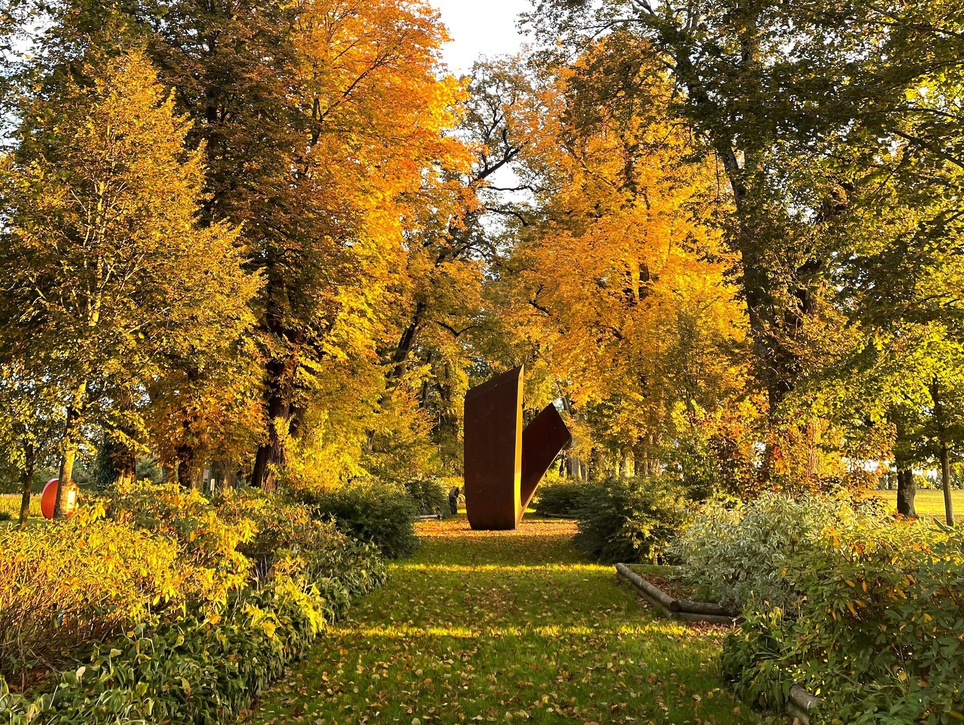 Vue large du jardin de Muni du Château de Vullierens au mois d'octobre avec des feuilles orangées au sol et sur les arbres.