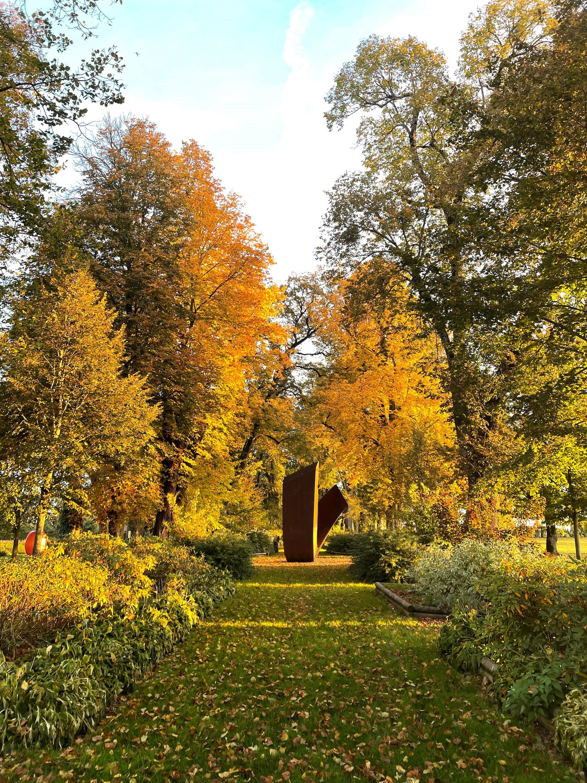 Vue large du jardin de Muni du Château de Vullierens au mois d'octobre avec des feuilles orangées au sol et sur les arbres.