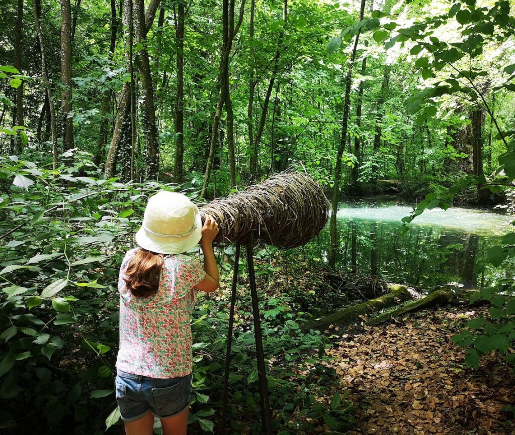 Fillette qui regarde à travers une longue vue en bois dans le Royaume du Roi Lézard, au Château de Vullierens.