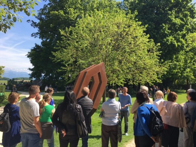 Groupe d'adultes écoutant le guide qui leur explique une sculpture d'Herbert Mehler lors d'une visite guidée en français.