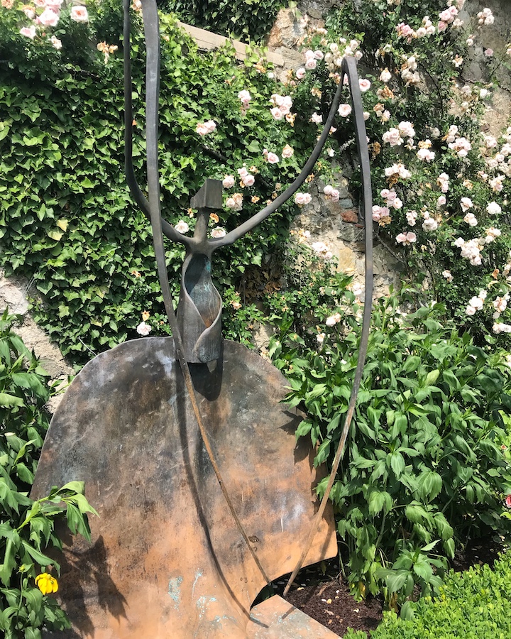 "Mante religieuse" est une sculpture de Manuel Torres, exposée contre un mur de rosiers.