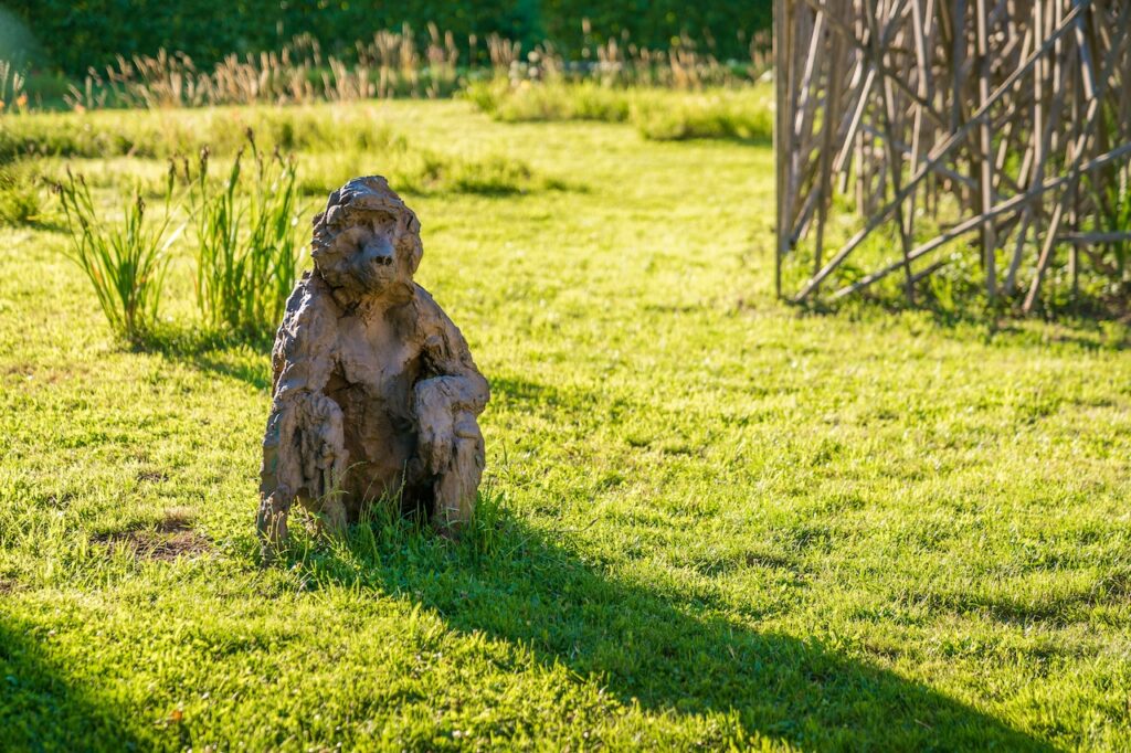 Sculpture représentant un petit singe assis dans l'herbe. Cette oeuvre est de Davide Rivalta, la lumière dorée de fin de journée l'éclaire.