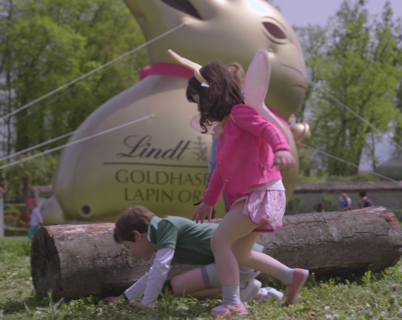 Un petit garçon et une petite fille en train de chercher des clochettes cachées dans les jardins lors de notre événement de Pâques, en collaboration avec Lindt. Il y a un immense lapin gonflable en arrière plan.